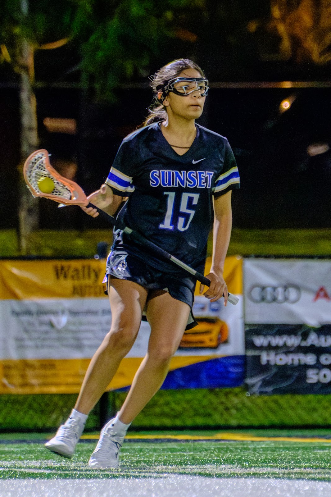 Sunset player wearing number 15 carrying the ball in a lacrosse stick.