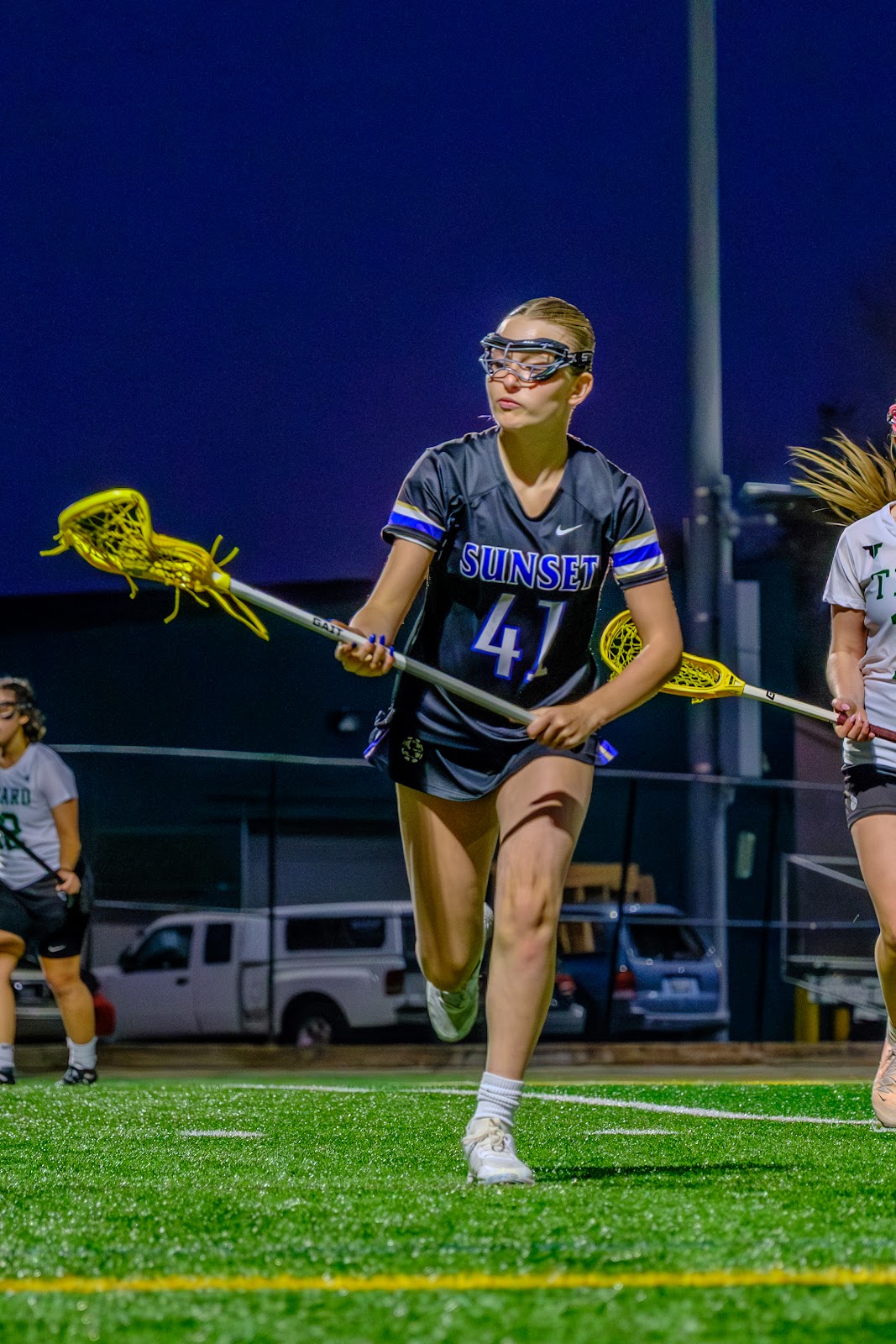 Sunset player wearing number 41 running with a lacrosse stick during an evening game.
