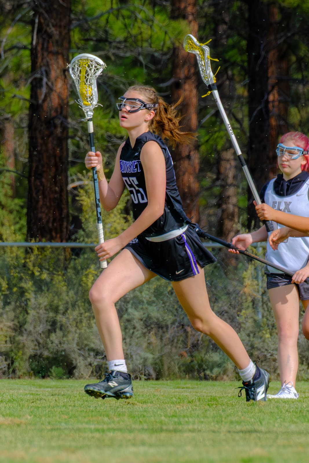 Sunset player wearing number 65 running upfield with a lacrosse stick during a daytime game.